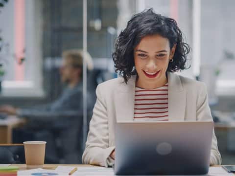 Young woman sitting in a conference room and smiling while looking at her laptop screen