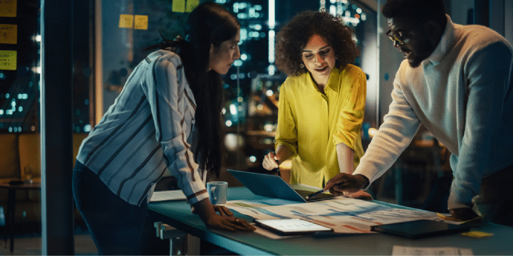 3 coworkers collaborating on a laptop in an office at night